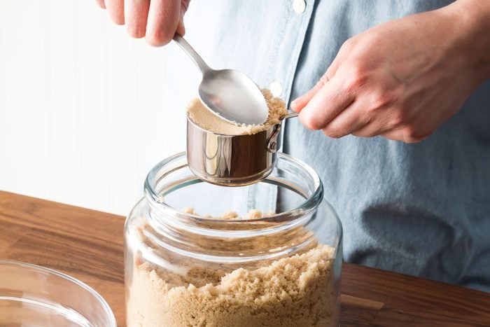 Anonymous Person Measuring Brown Sugar from a glass container in a kitchen