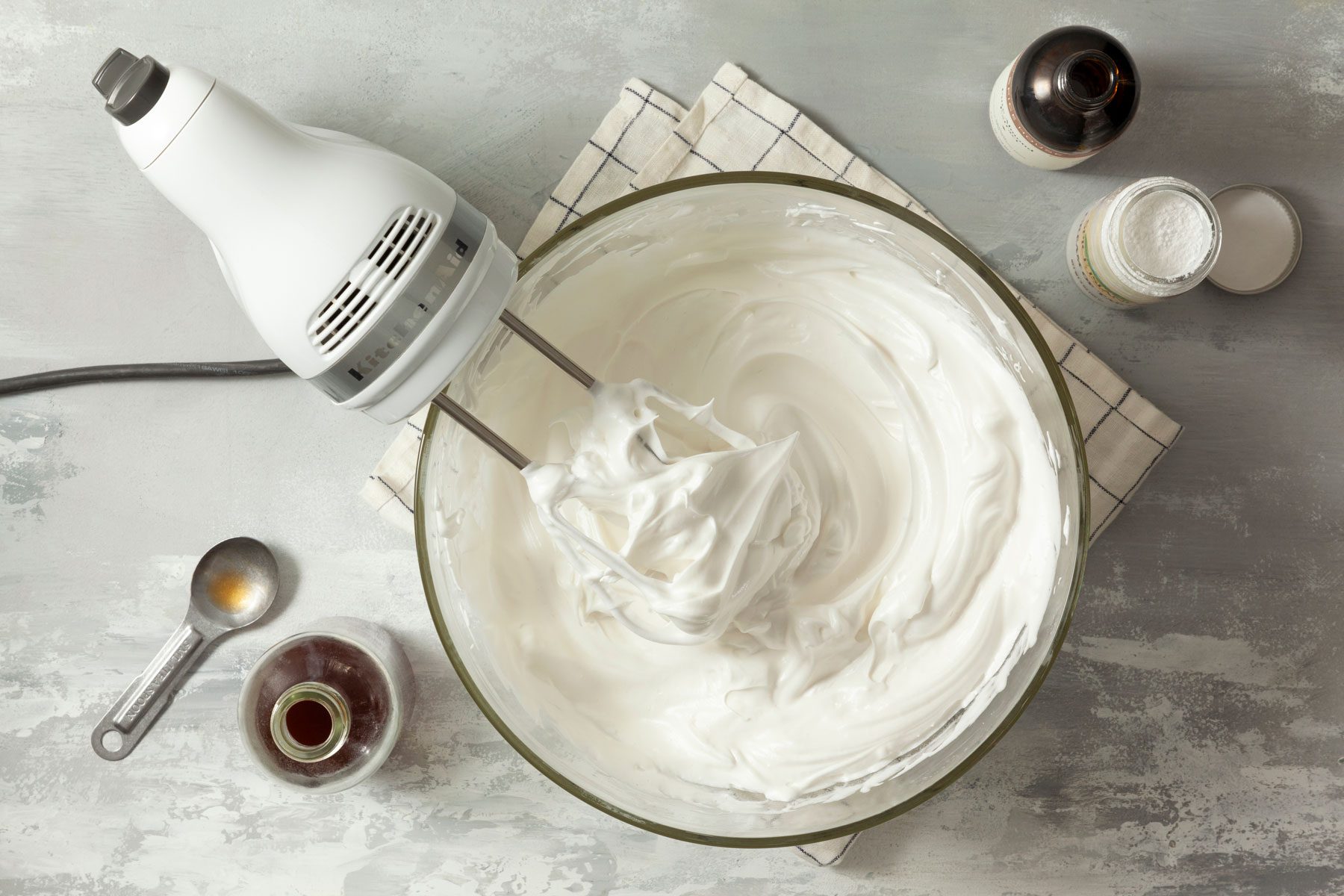 White cream in a large bowl with a hand blender placed on a marble countertop