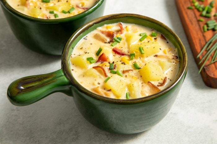A close-up of two green bowls filled with corn chowder with bacon soup