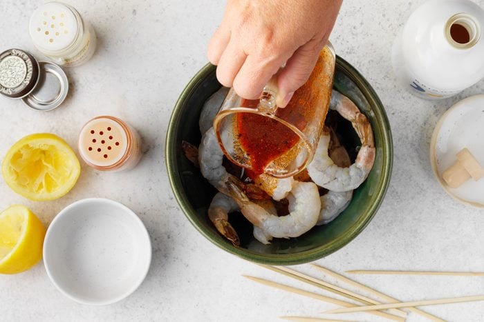 A hand pouring sauce into a bowl of shrimp