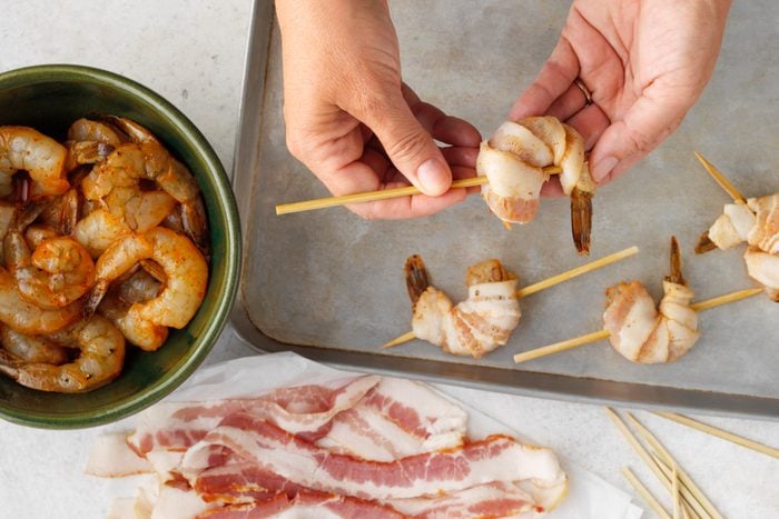 A person holding a stick with bacon wrapped shrimp