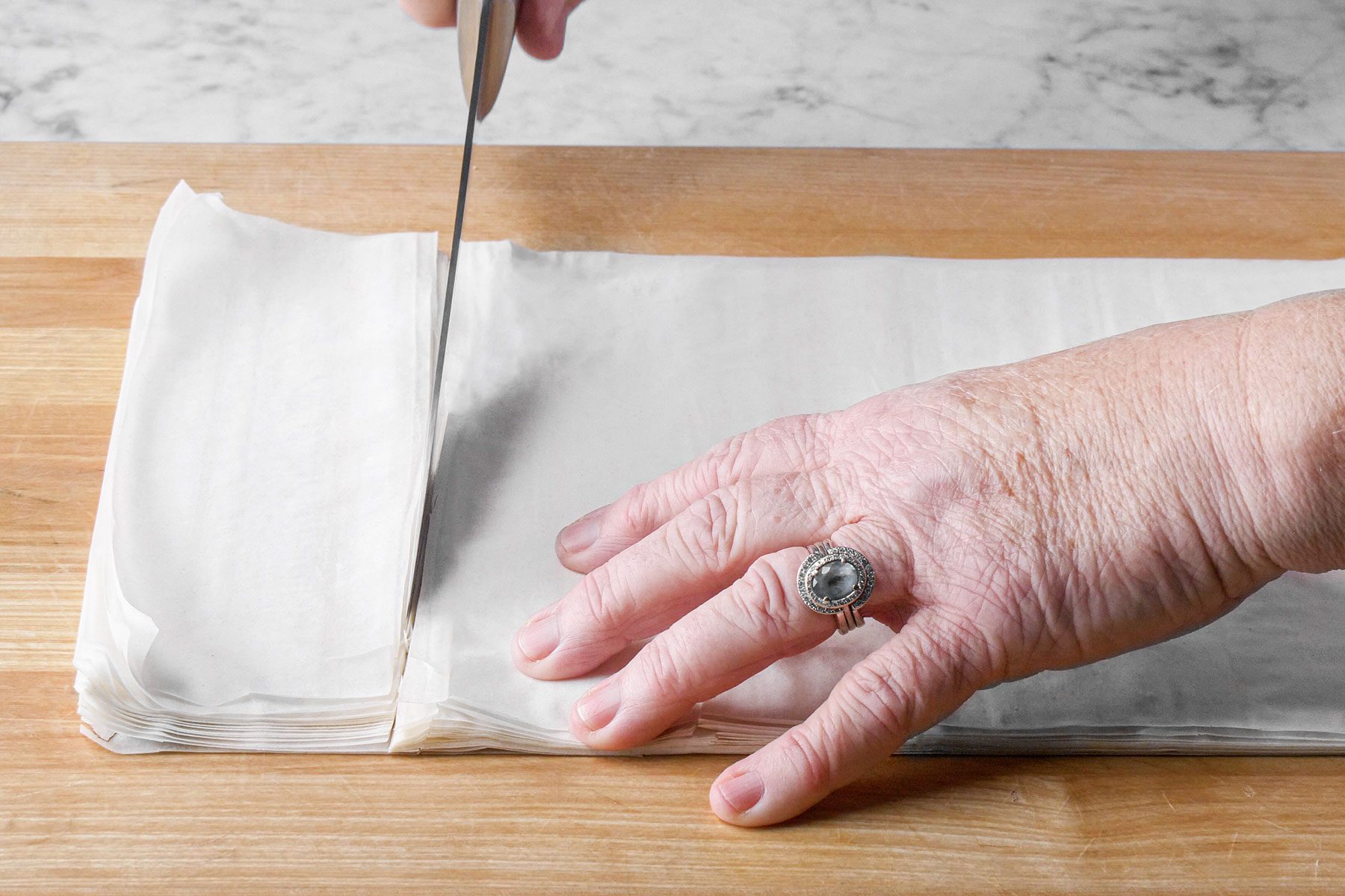 Cutting phyllo dough sheets with knife on wooden board