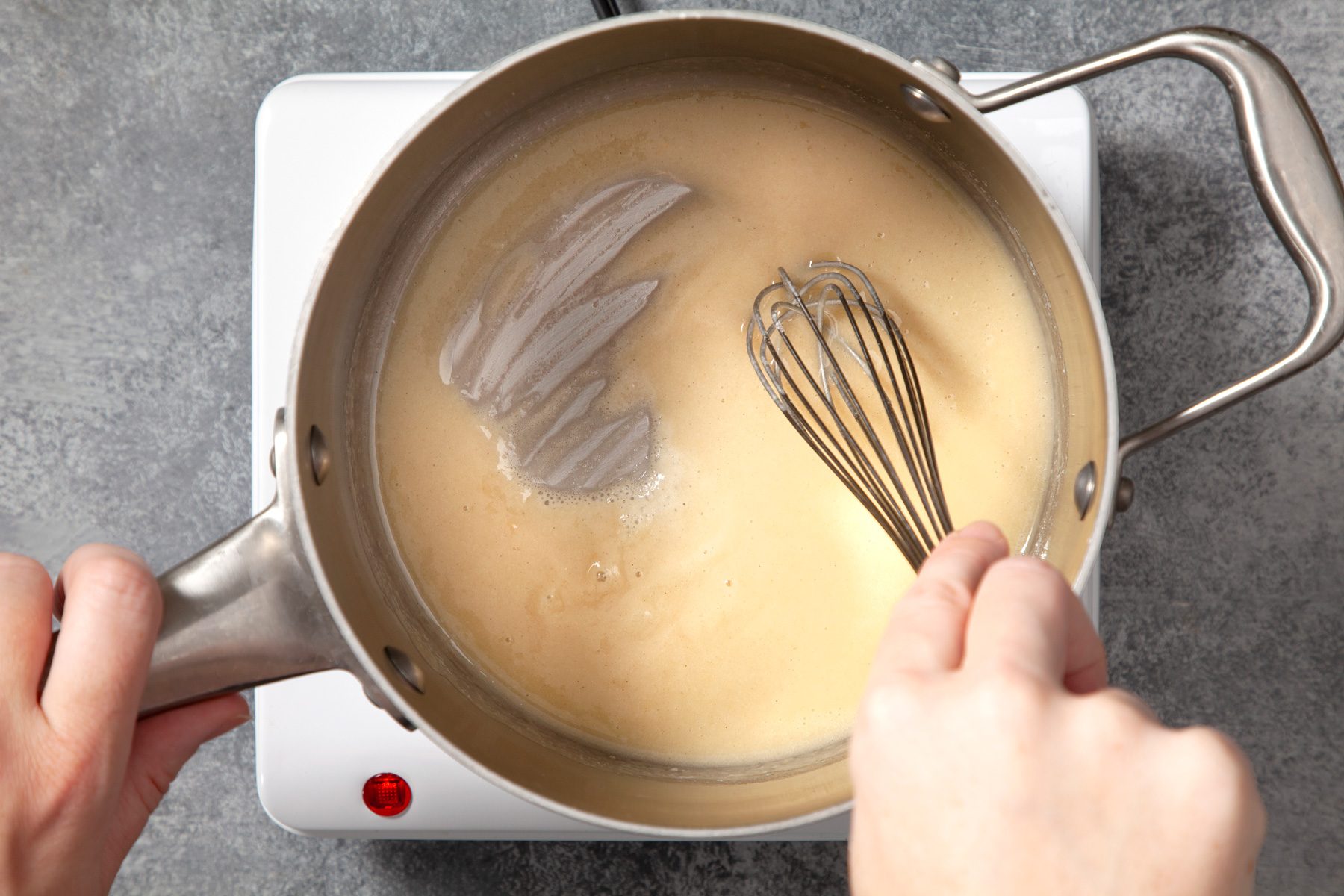 A hand holding a saucepan and whisking the mixture with the other hand
