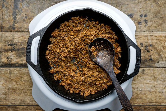 cooking ground beef in a cast iron skillet on an induction cooktop on wooden surface