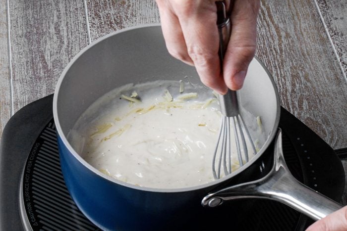 Whisking cheese and milk mixture in a small sauce pan
