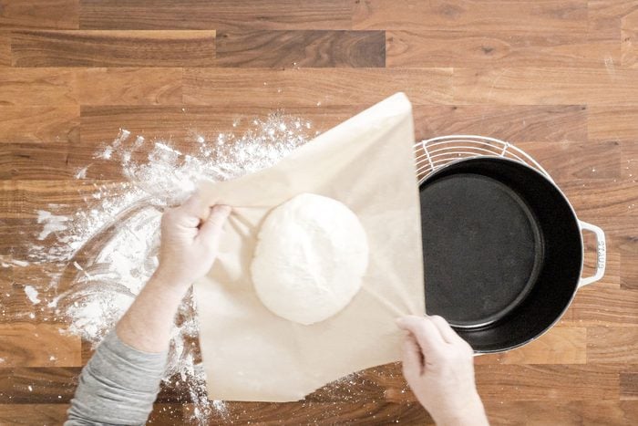 Lowering the dough with help of parchment paper into heated oven pot