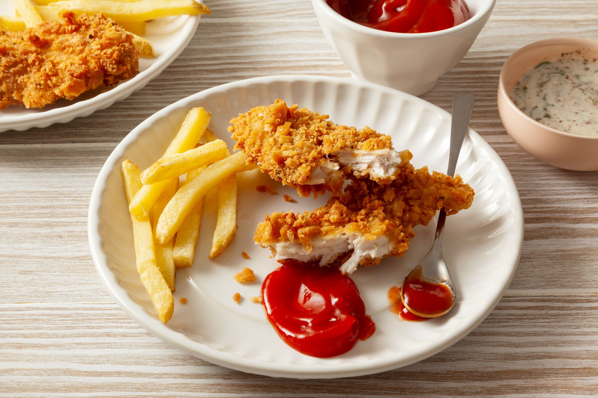 Fried Chicken Strips Served In A White Plate with Some French Fries and Tomato Ketchup