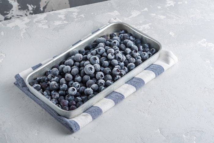 Frozen blueberries in a metal tray on a concrete background.