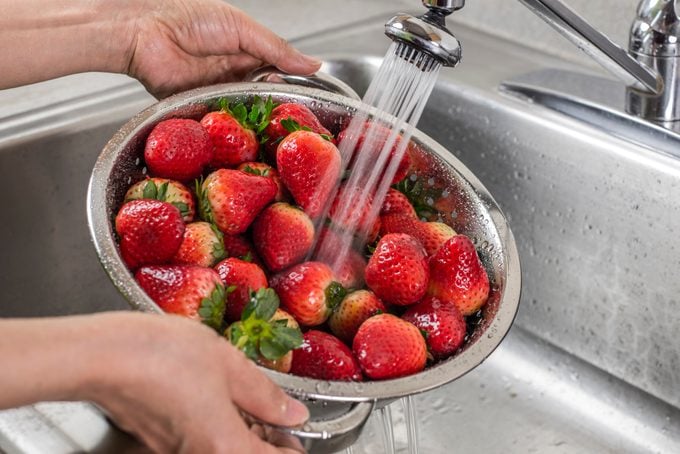 A silver colander full of strawberries being rinsed