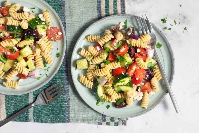 Greek Pasta Salad in a plate with fork on a marble countertop