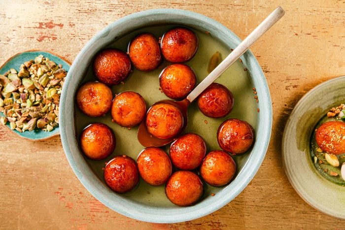 a lot of Gulab Jamun in a saucepan of sugar syrup on wooden surface