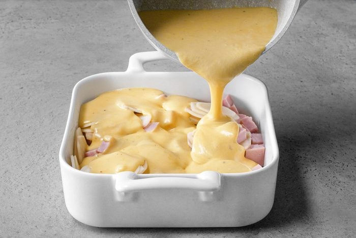 Pouring cheese sauce over Ham and Potato