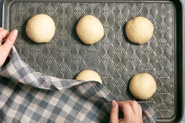 Covering dough balls with cloth on baking tray