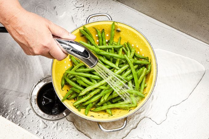 Overhead Shot Of Rinsing Green Beans Under Cold Water In Kitchen Sink