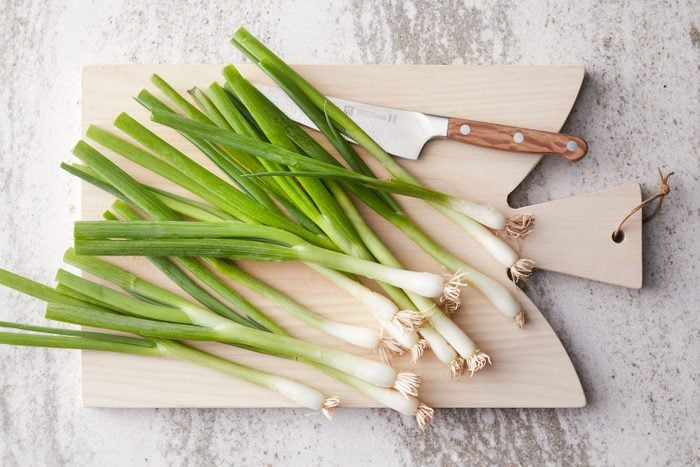 green onions on a cutting board with a knife on a kitchen counter