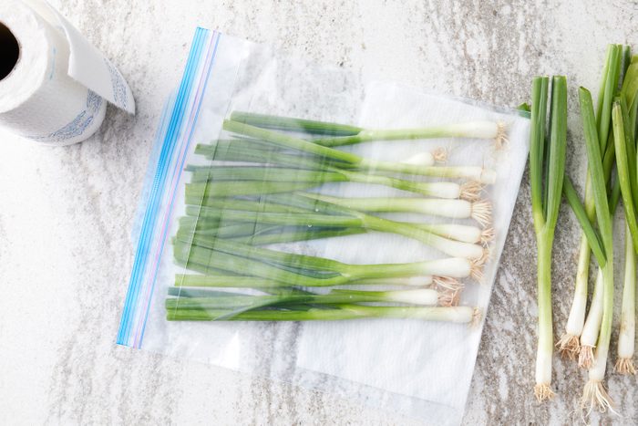 green onions prepped for storage in a plastic bag with a damp paper towel 