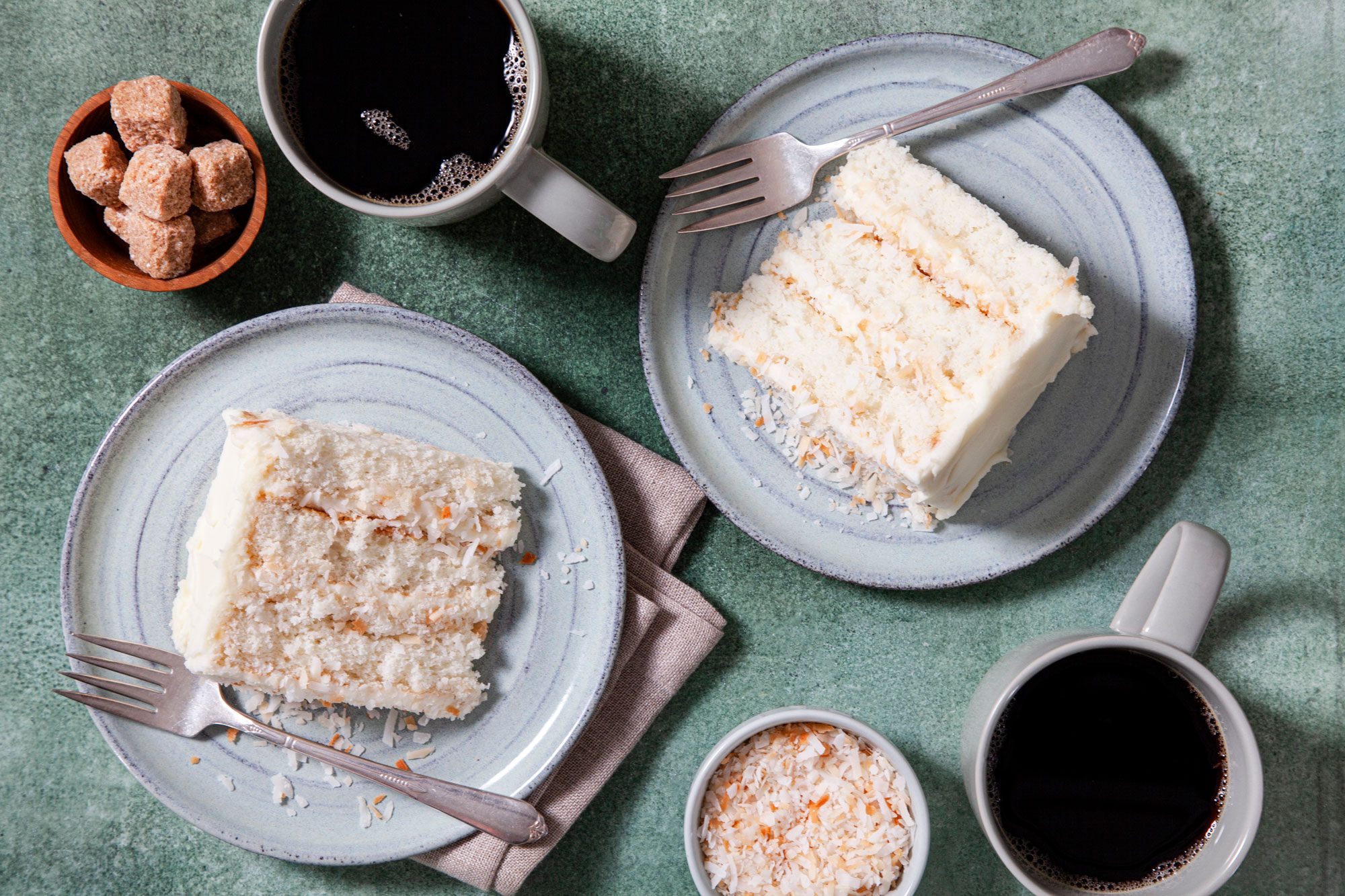 Two slices of Incredible Coconut Cake on a plate, accompanied by two cups of coffee