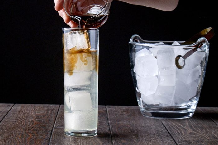 Pouring cola in a highball glass full with ice cubes, vodka and gin
