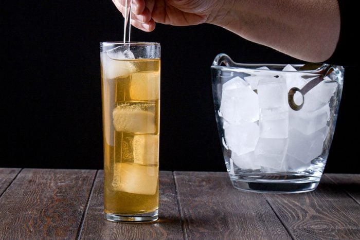 a person's hand stirs Long Island Iced Tea in a glass using a glass stirring rod