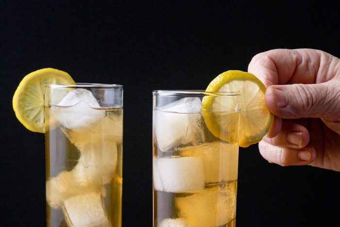 a person's hand garnishing a glass of Long Island Iced Tea with a lemon slice