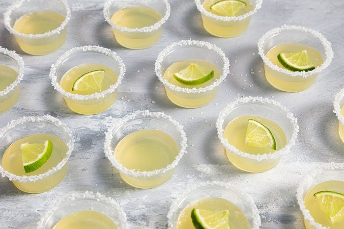 Margarita Jell O Shots served in small cups with lemon wedges on them and salt garnished on the rim of the cup