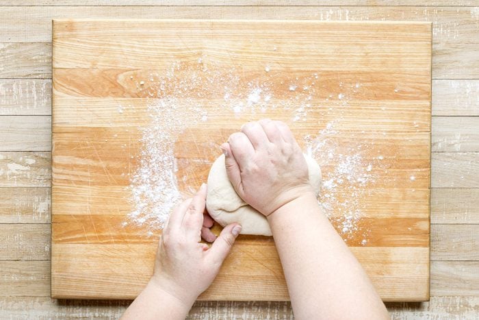 A person's hands kneading dough on a wooden surface.
