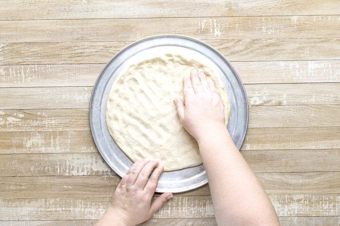 A person's hands rolling out dough on a metal plate