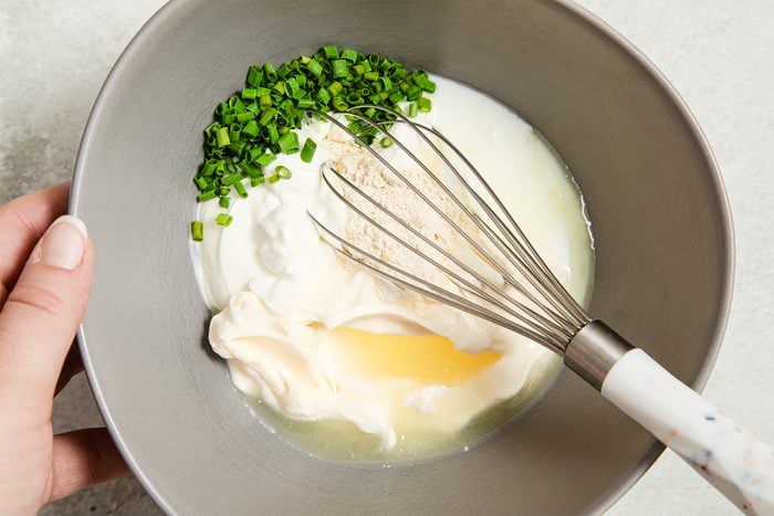 A whisk and a bowl of cream and green onions
