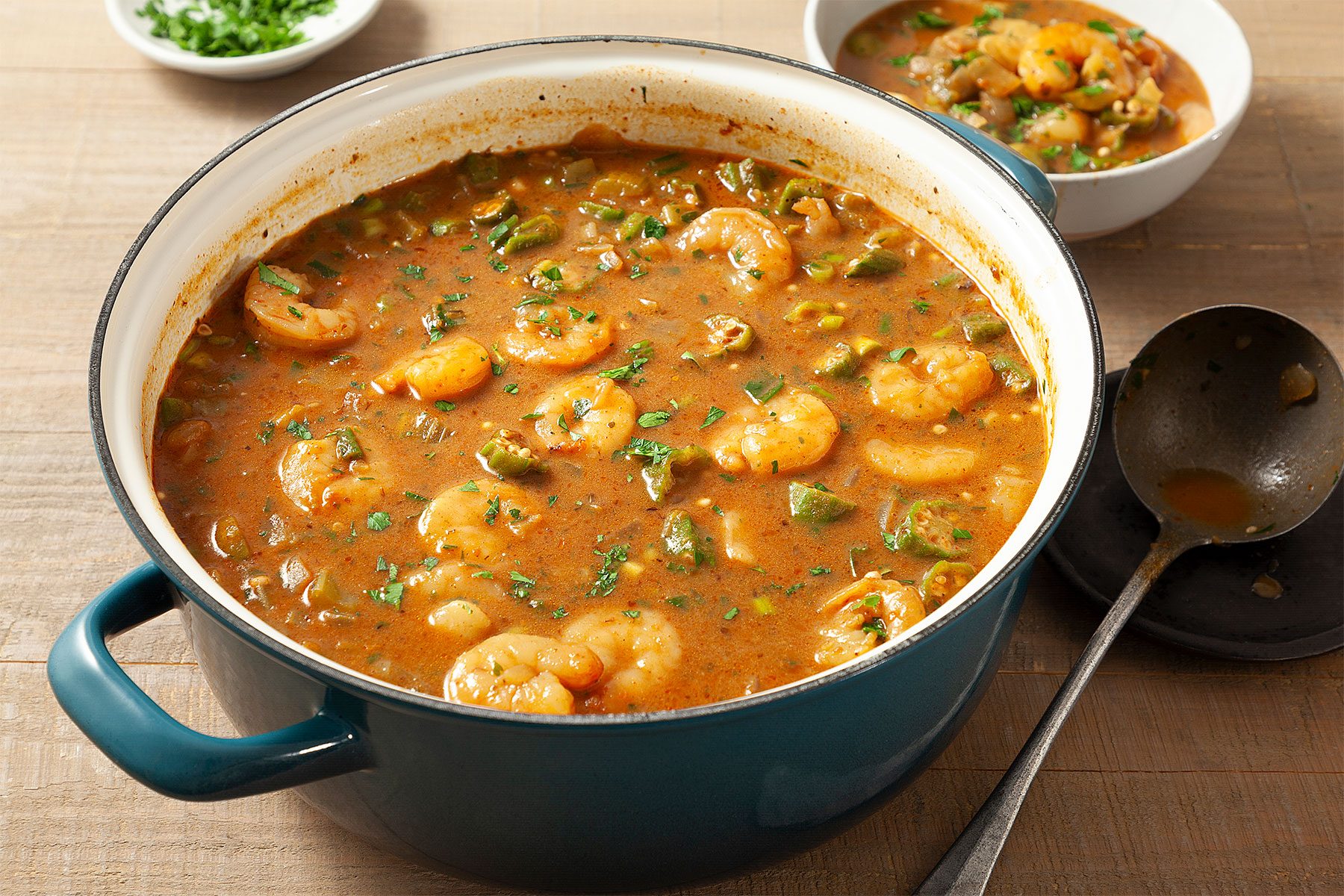 3/4th shot; wooden background; Seafood Gumbo; in blue serving bowl; with big serving spoon; Seafood Gumbo; in small white bowl; parsley; in small white bowl;