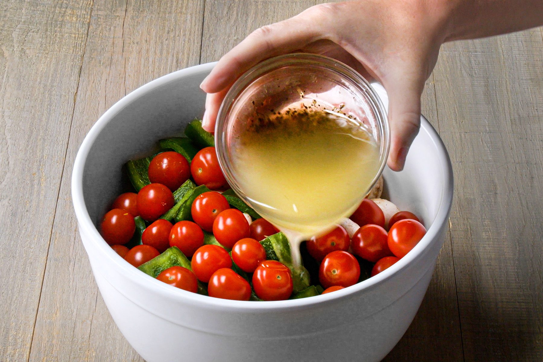 Pouring salad dressing on vegetables in a large bowl