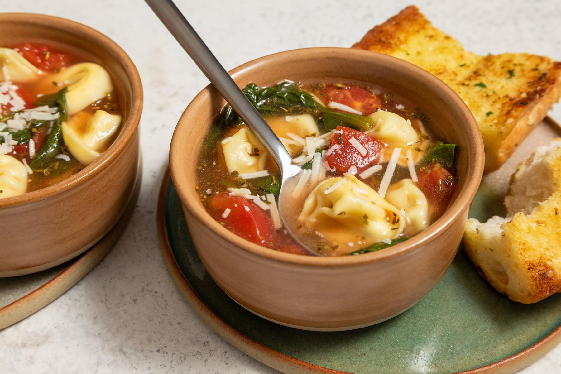A bowl of spinach tortellini soup with a spoon