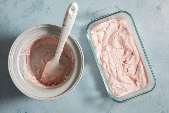 Strawberry ice cream in a container beside a big empty bowl