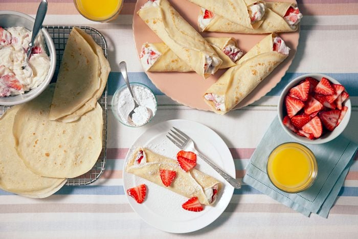 A plate of delicious strawberry crepes topped with confectioners' sugar and served with strawberries and juice