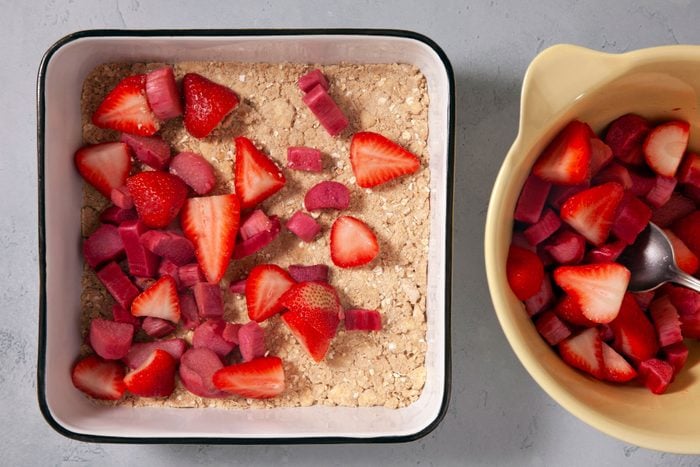 Rhubarb and strawberries arranged on crumble mixture in a baking pan