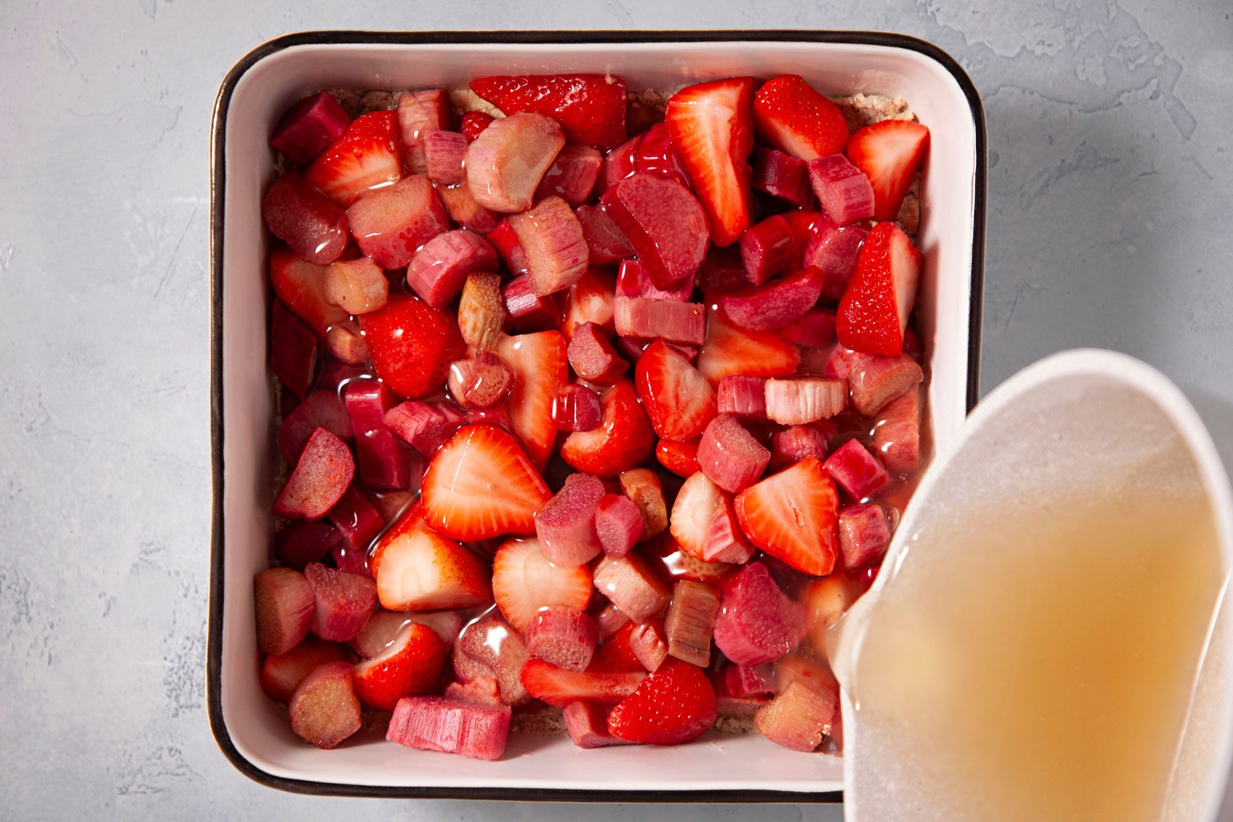 Pouring the sugar mixture over the strawberries in a large baking pan