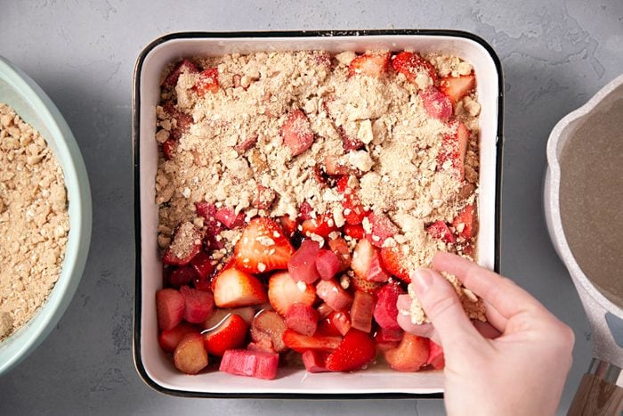Sprinkling the crumb mixture over the strawberries in a large baking pan