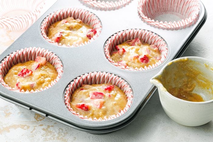 A muffin tin with a cup of Strawberry Rhubarb batter