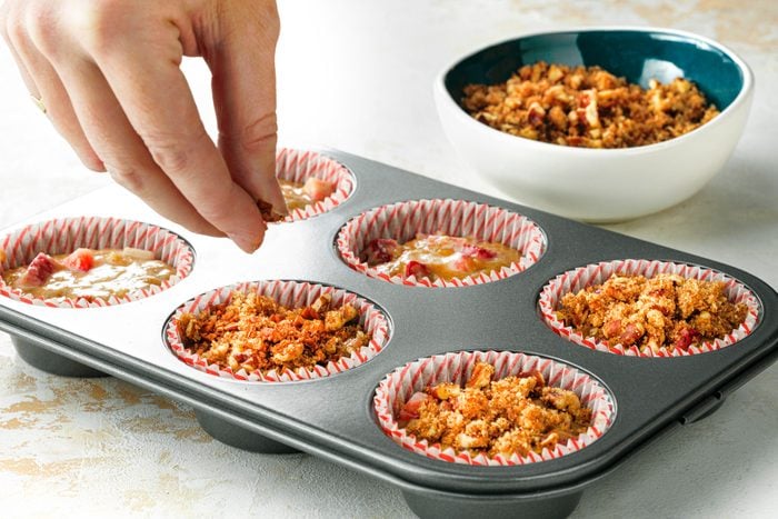 A person putting crumbles in a muffin tin