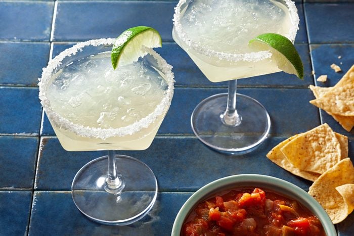 Two virgin margaritas and a bowl of salsa on a blue tile floor
