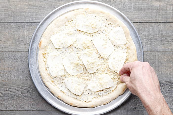 sprinkling parmesan cheese on pizza base