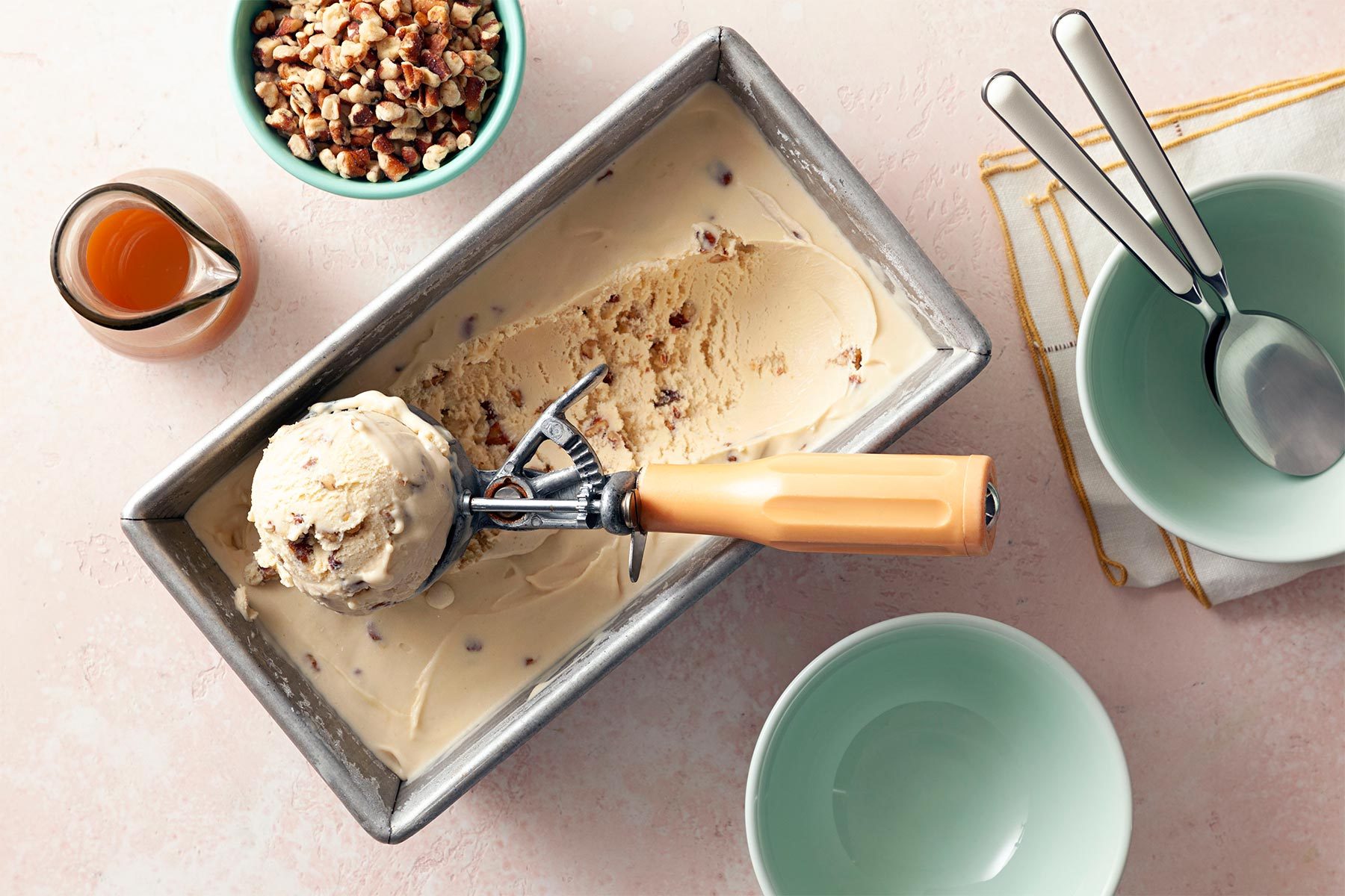 overhead shot of butter pecan ice cream in a pan; scoop; chopped pecans; caramel suace;