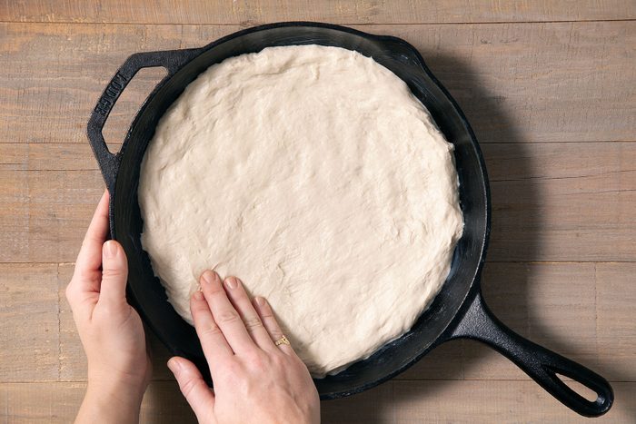 pressing pizza dough on cast iron