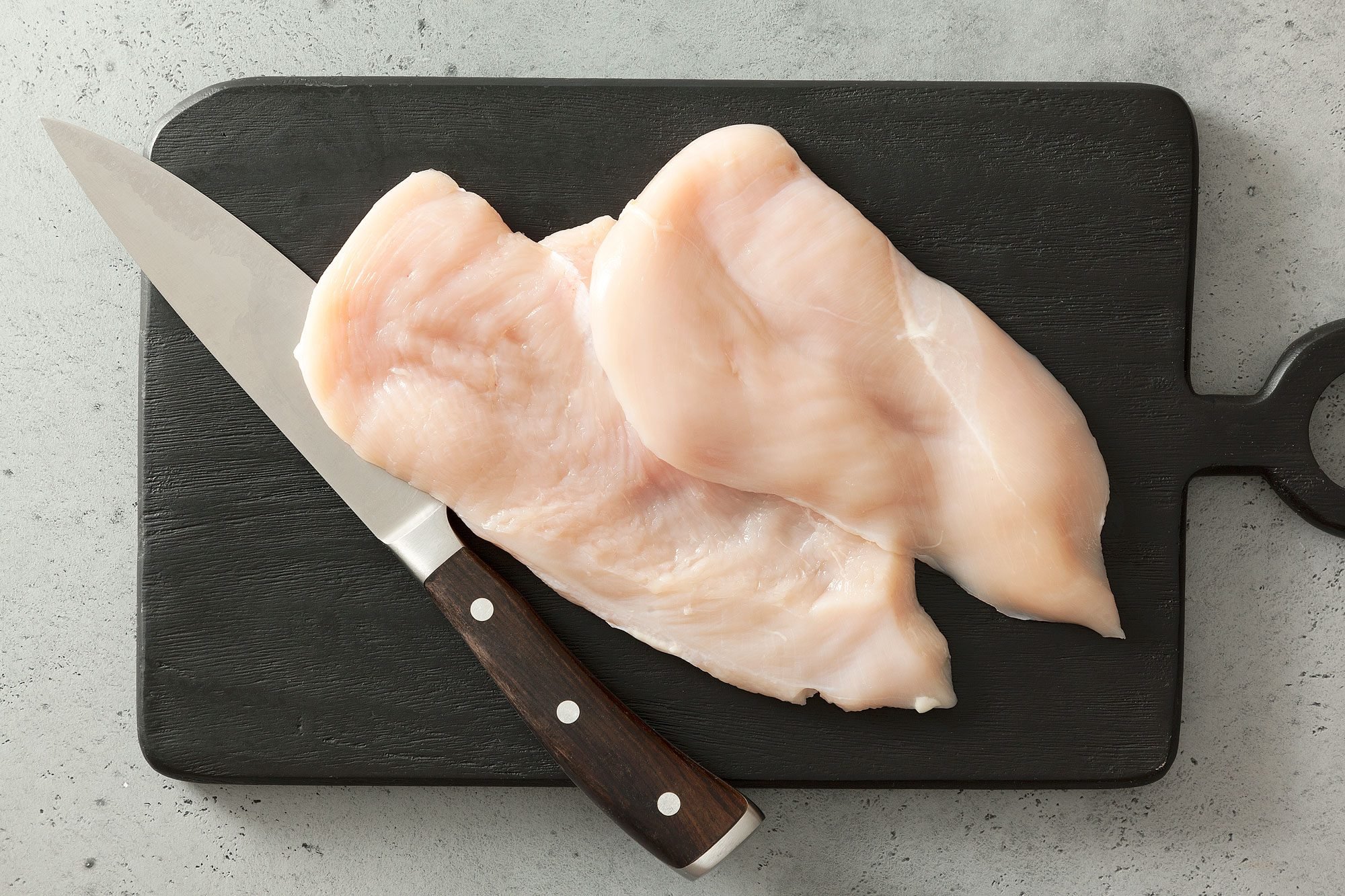 Chicken Breasts and a Knife on Chopping Board on Grey Surface