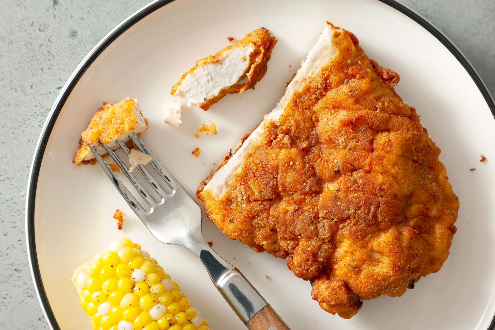 Crispy Fried Chicken Breasts Served with Boiled Corn on a Small Plate on a Grey Surface