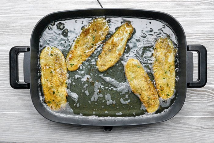 Frying bread crumbs covered eggplant slices in skillet