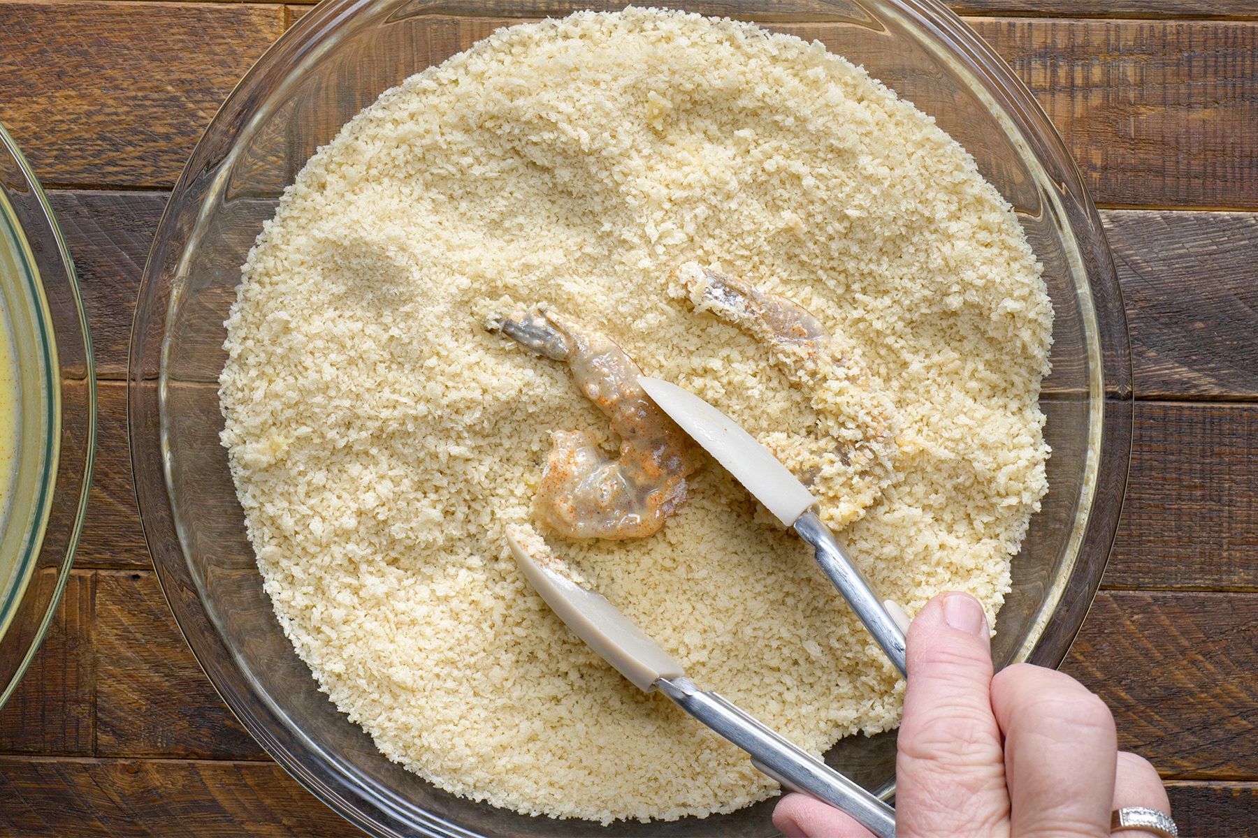 A person coating shrimp in bread crumbs