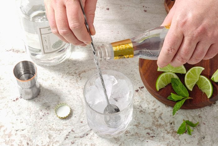 Pouring tonic water in glass filled with ice and Gin