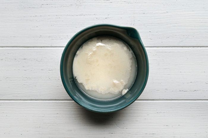 yeast, sugar and warm water in a bowl on white painted wooden surface