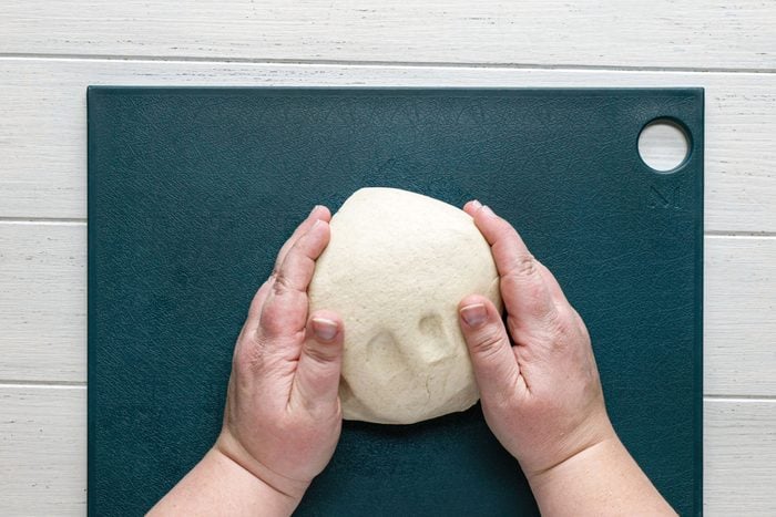 A Person's Hands Holding Pizza Crust Dough on a Chopping Board