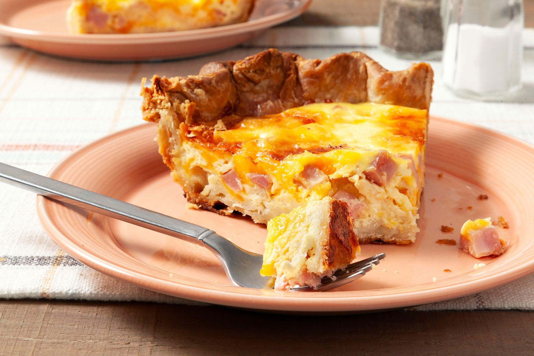 Slice of Ham And Cheese Quiche on plate with fork